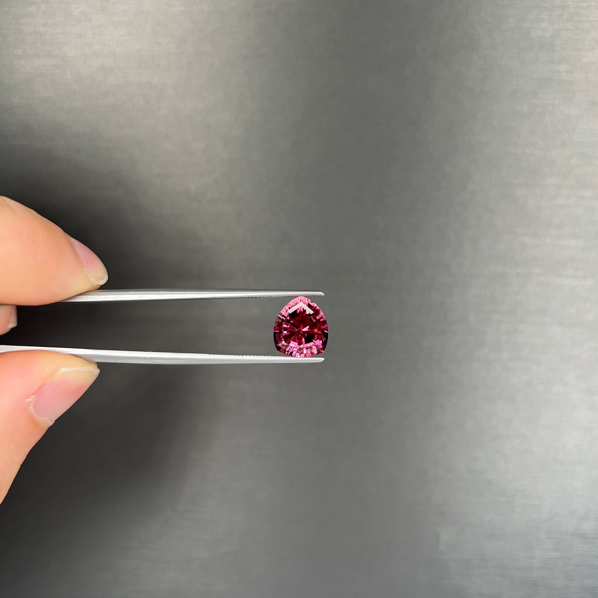 A loose, rounded trillion shield cut pink tourmaline gemstone.