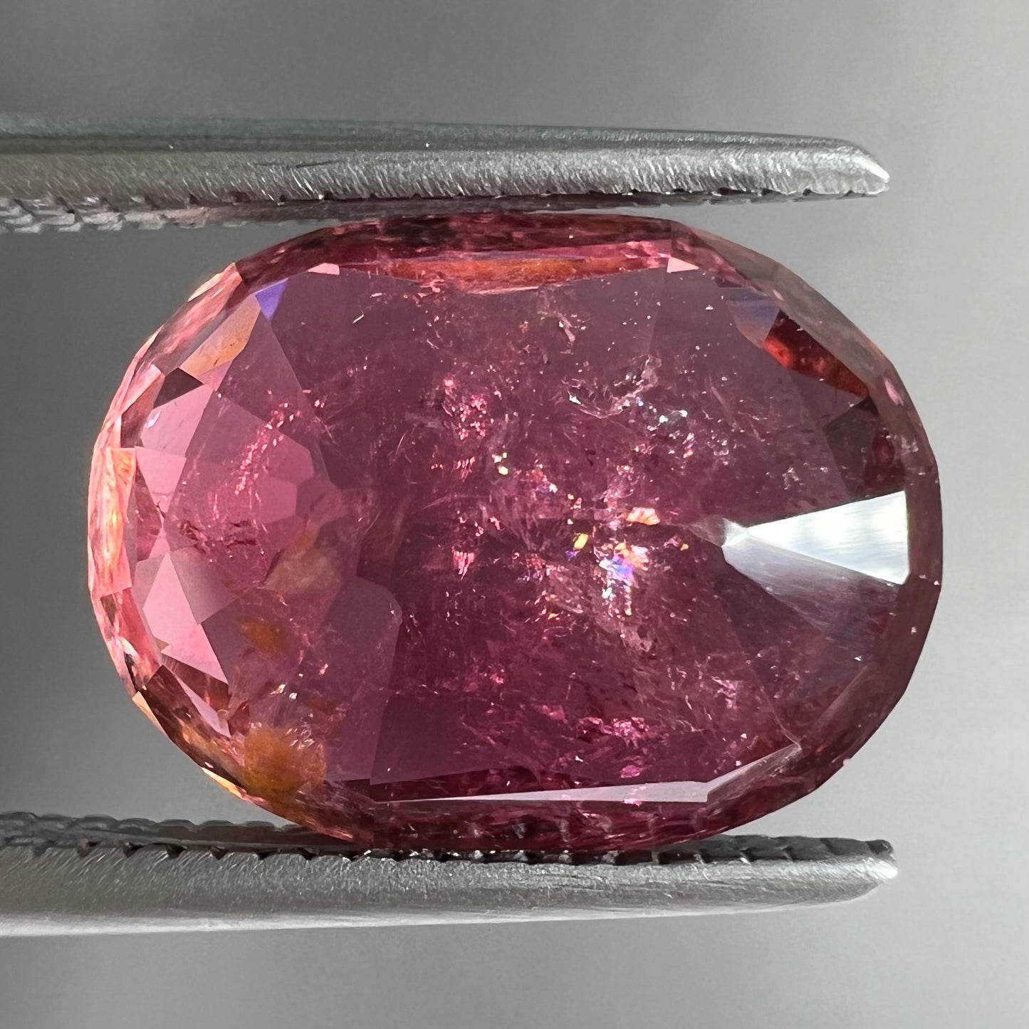 A faceted, oval cut, melon pink tourmaline gemstone.