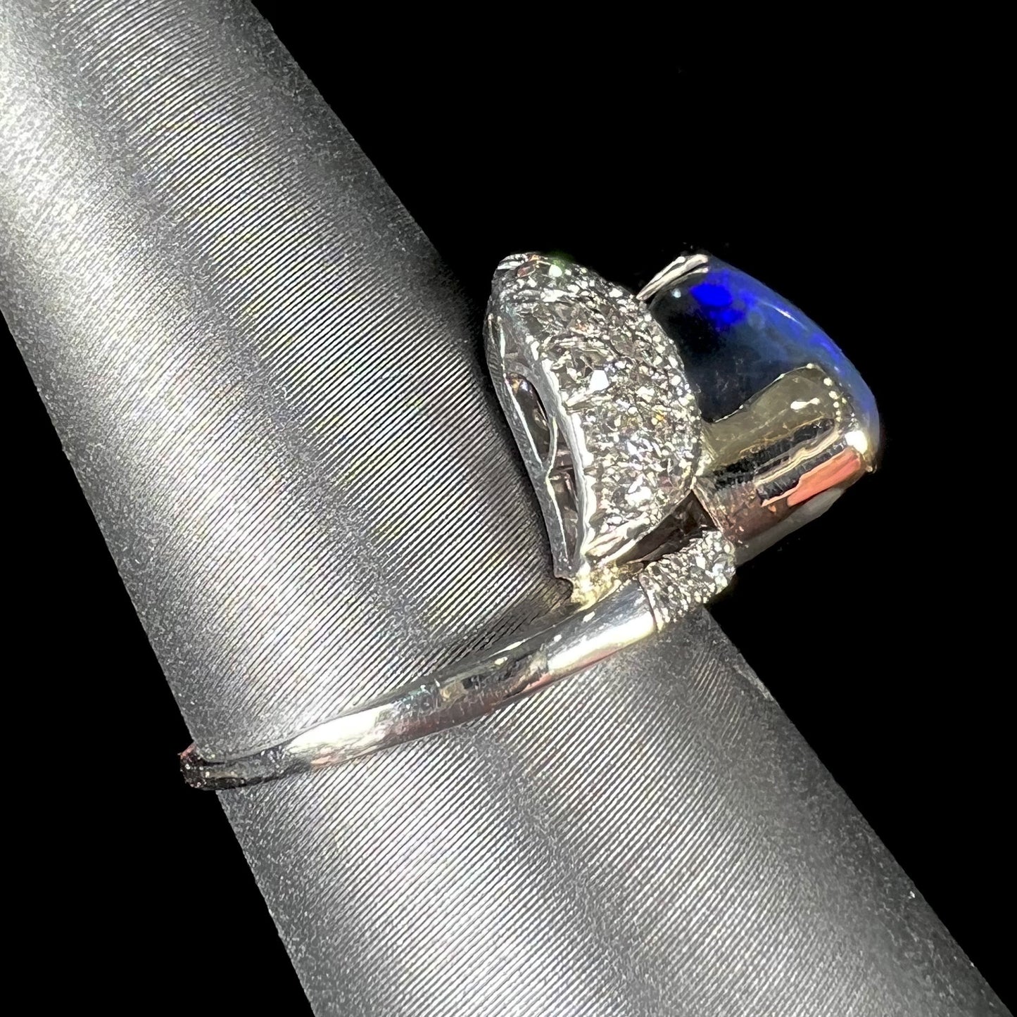 A platinum ring set with an oval cut black opal and round cut diamonds in a leaf design.