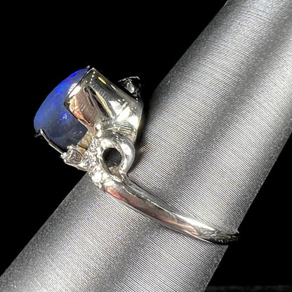 A platinum ring set with an oval cut black opal and round cut diamonds in a leaf design.