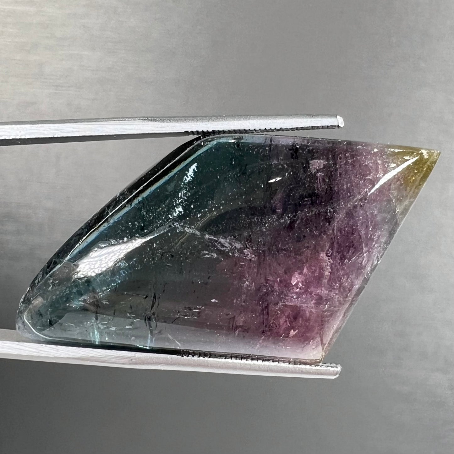 A loose, freeform cabochon cut tricolor tourmaline stone that has blue, pink, and yellow colors.