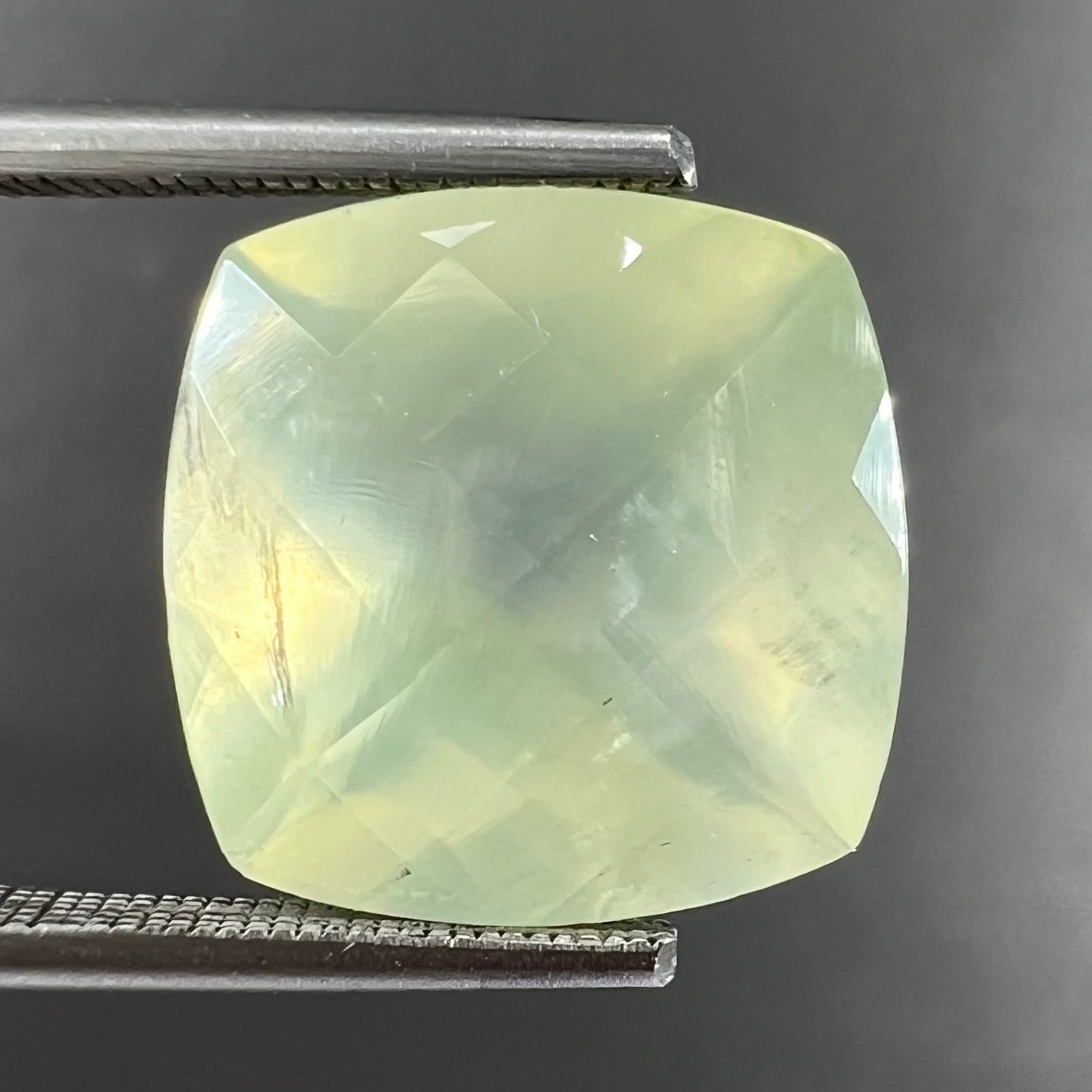 A loose, faceted checkerboard cushion cut green prehnite stone.  The stone is sleepy yellowish green.