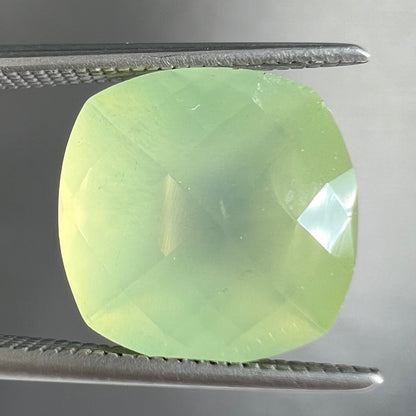 A loose, checkerboard cushion cut prehnite gemstone.  The stone is a sleepy yellow green color.