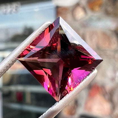 A loose, faceted princess cut tourmaline gemstone.  The stone is a burgundy purple color.