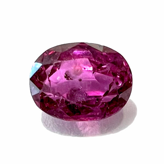 A loose, faceted oval cut natural purple sapphire.  The stone has a burst crystal inclusion.