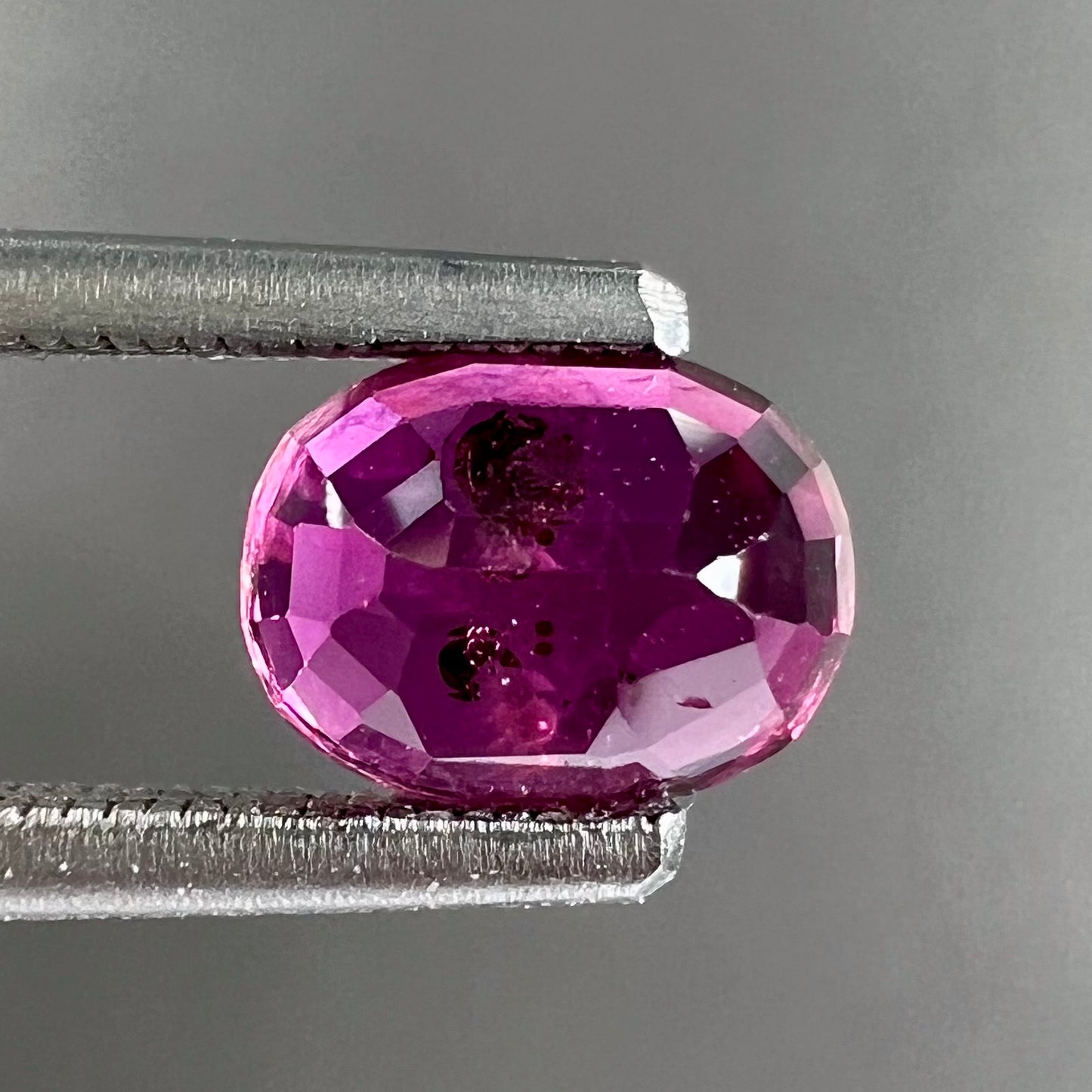 A loose, faceted oval cut natural purple sapphire.  The stone has a burst crystal inclusion.