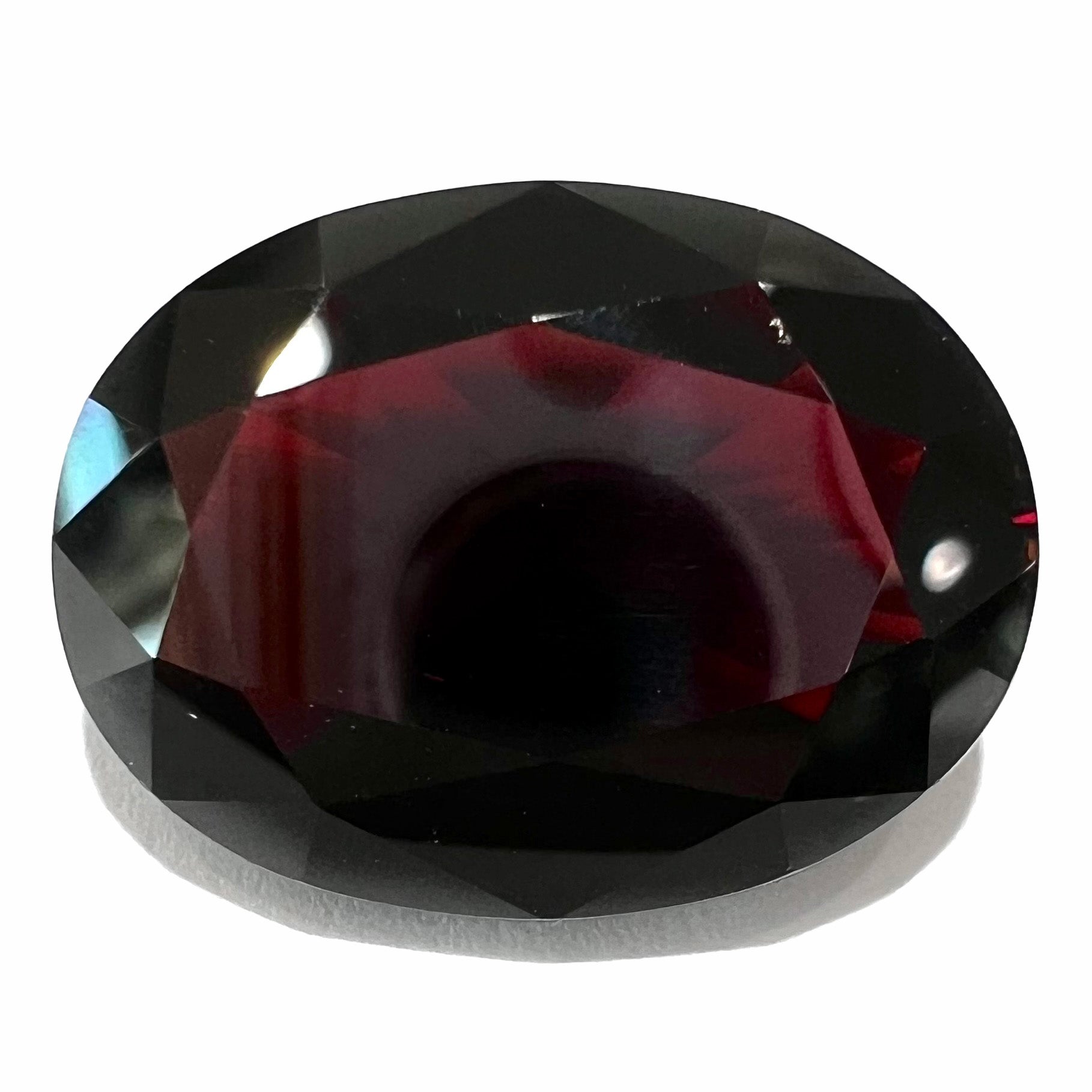 A loose, faceted oval cut pyrope garnet gemstone.  The stone is a deep, dark red color.