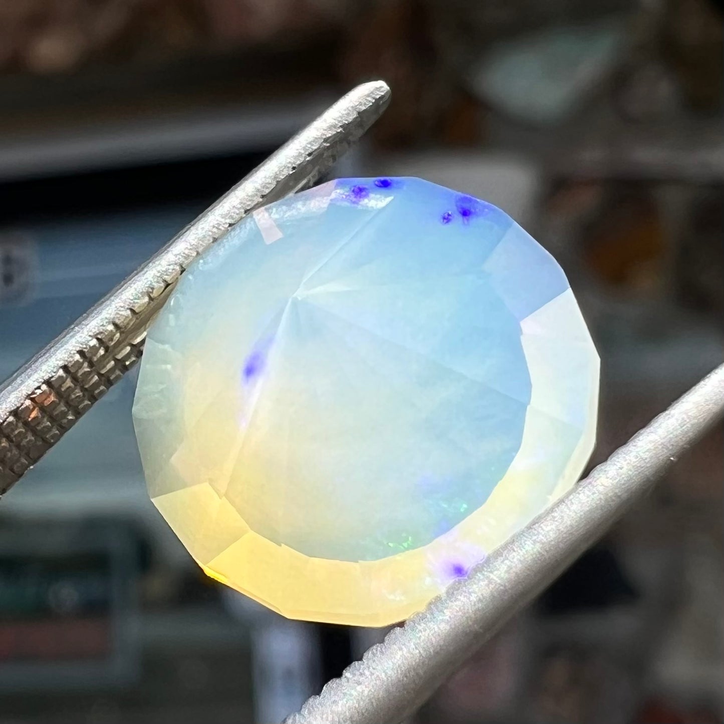 A loose, modified round cut Mexican fire opal gemstone.  The stone is transluscent light yellow with green and blue fire.