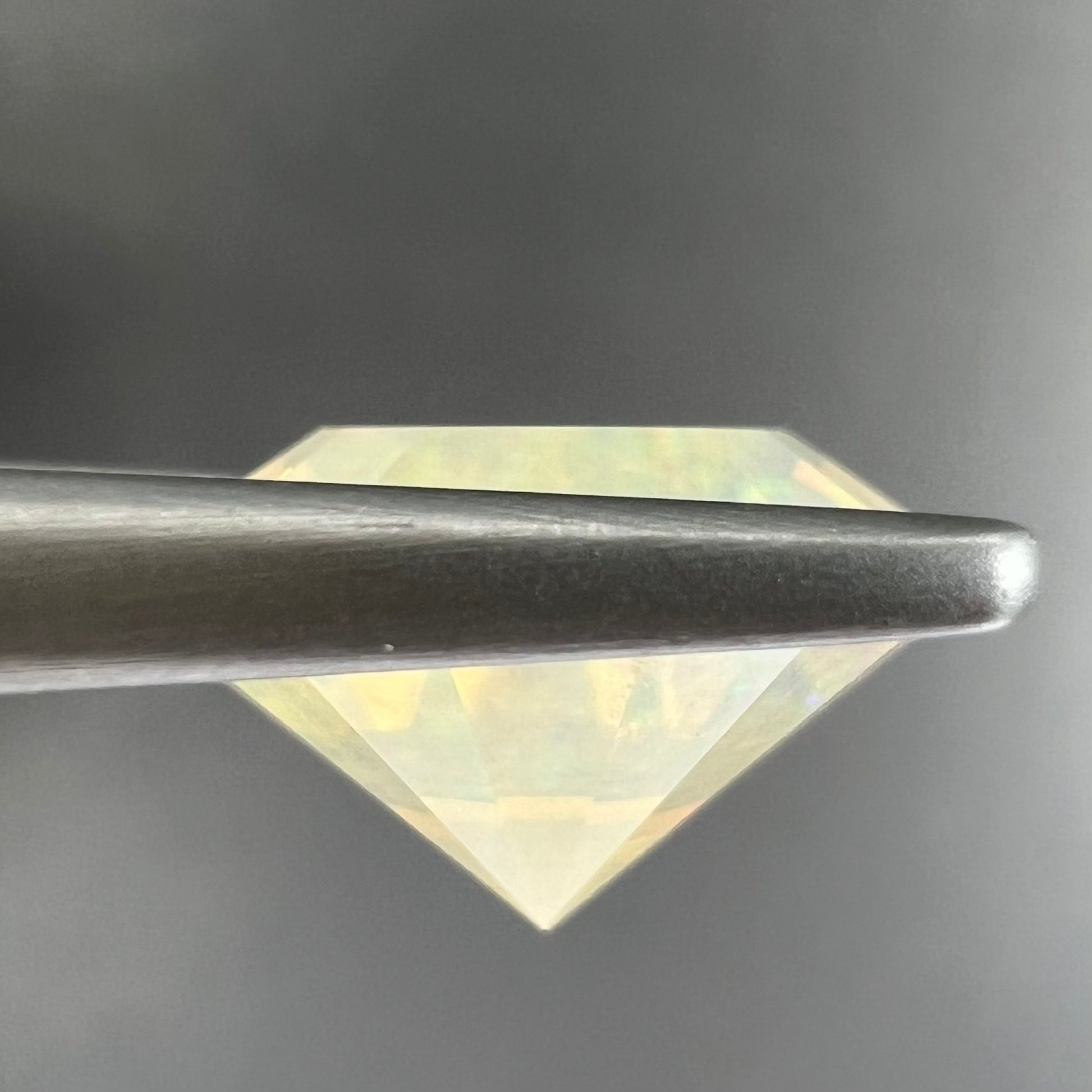 A loose, round faceted Mexican fire opal gemstone.  The stone is transluscent light orange color with rainbow play of color in the sunlight.