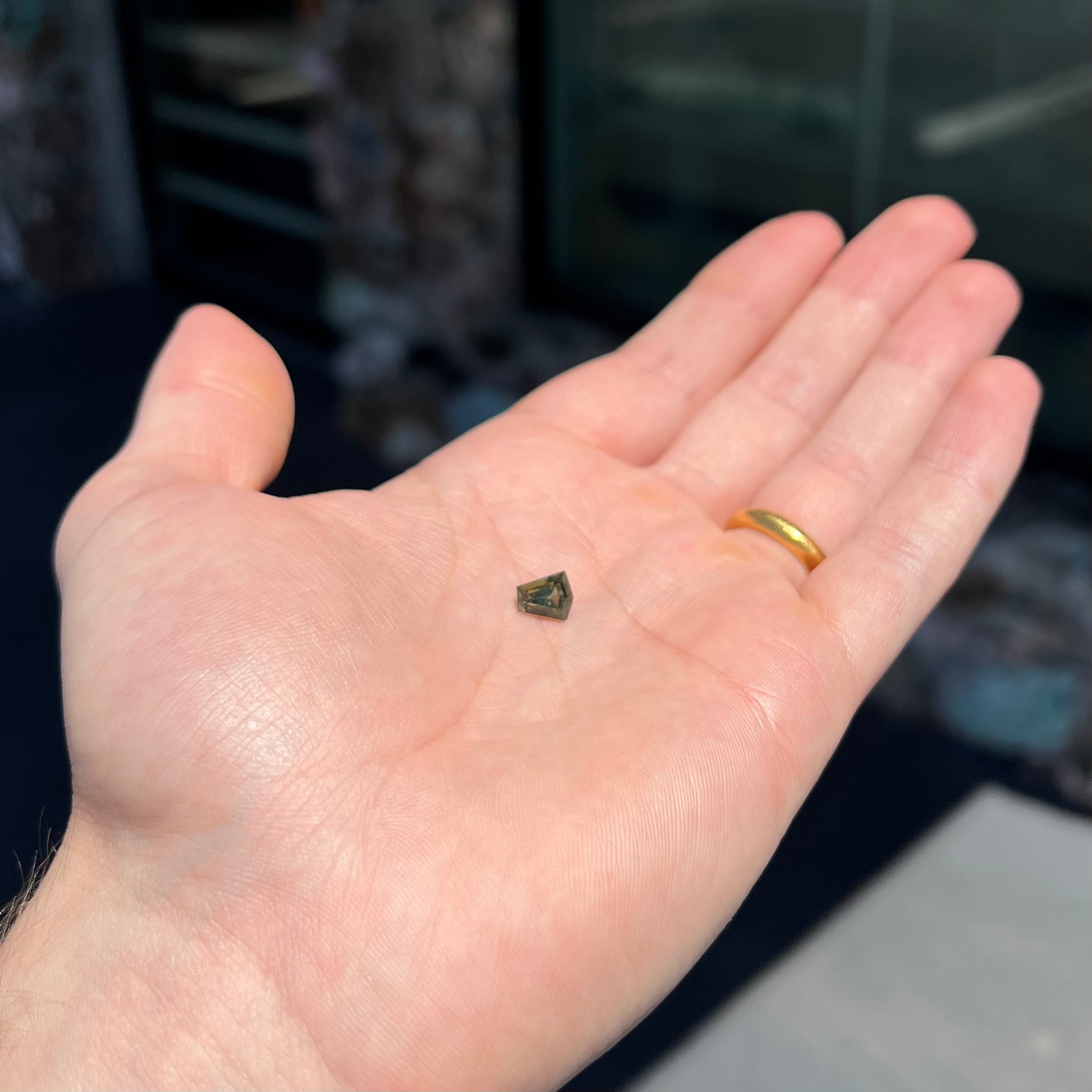 A loose, shield cut, natural moldavite gemstone.  The stone has a small chip in the top corner facet.