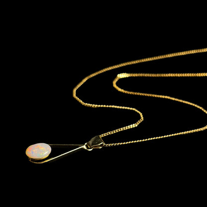 An oval cabochon cut natural white crystal opal set into a gold plated necklace.