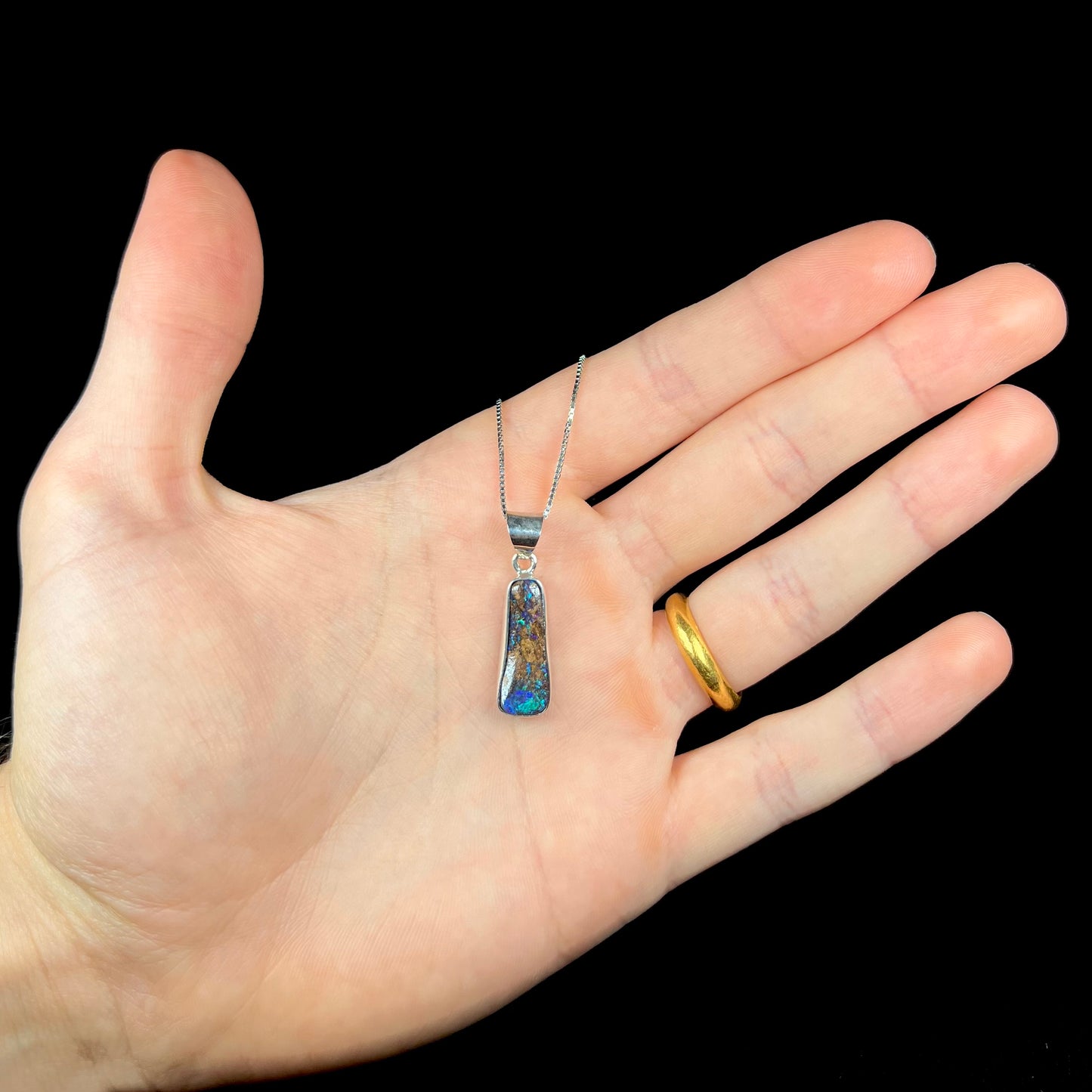 A sterling silver necklace bezel set with a natural Australian boulder opal stone.  The stone shines colors of blue, green, and purple.