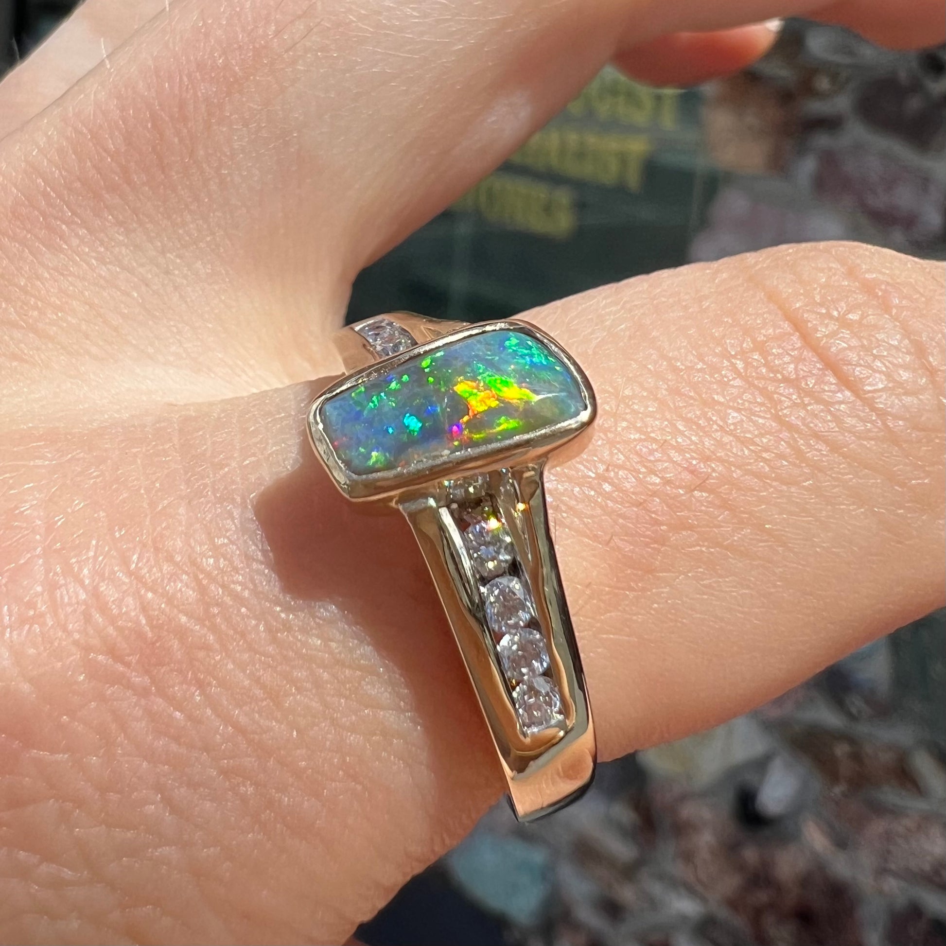 A ladies' yellow gold Australian black crystal opal ring channel set with diamond accent stones.