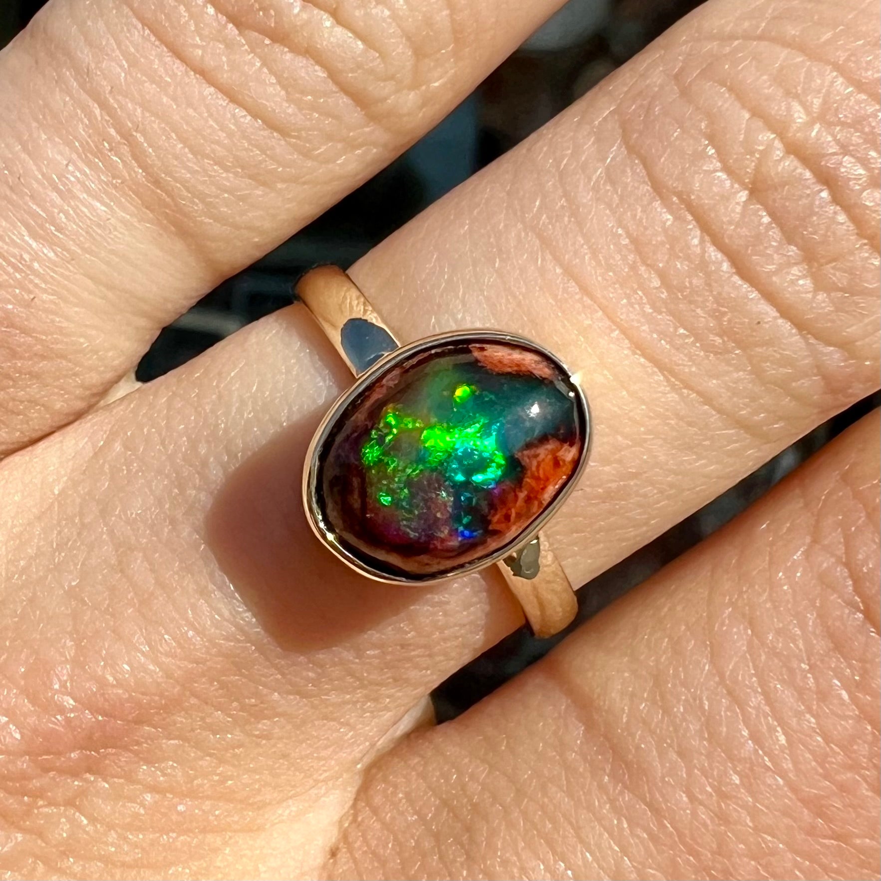 A ladies' yellow gold solitaire ring bezel set with an oval cabochon cut natural black Mexican cantera fire opal stone.