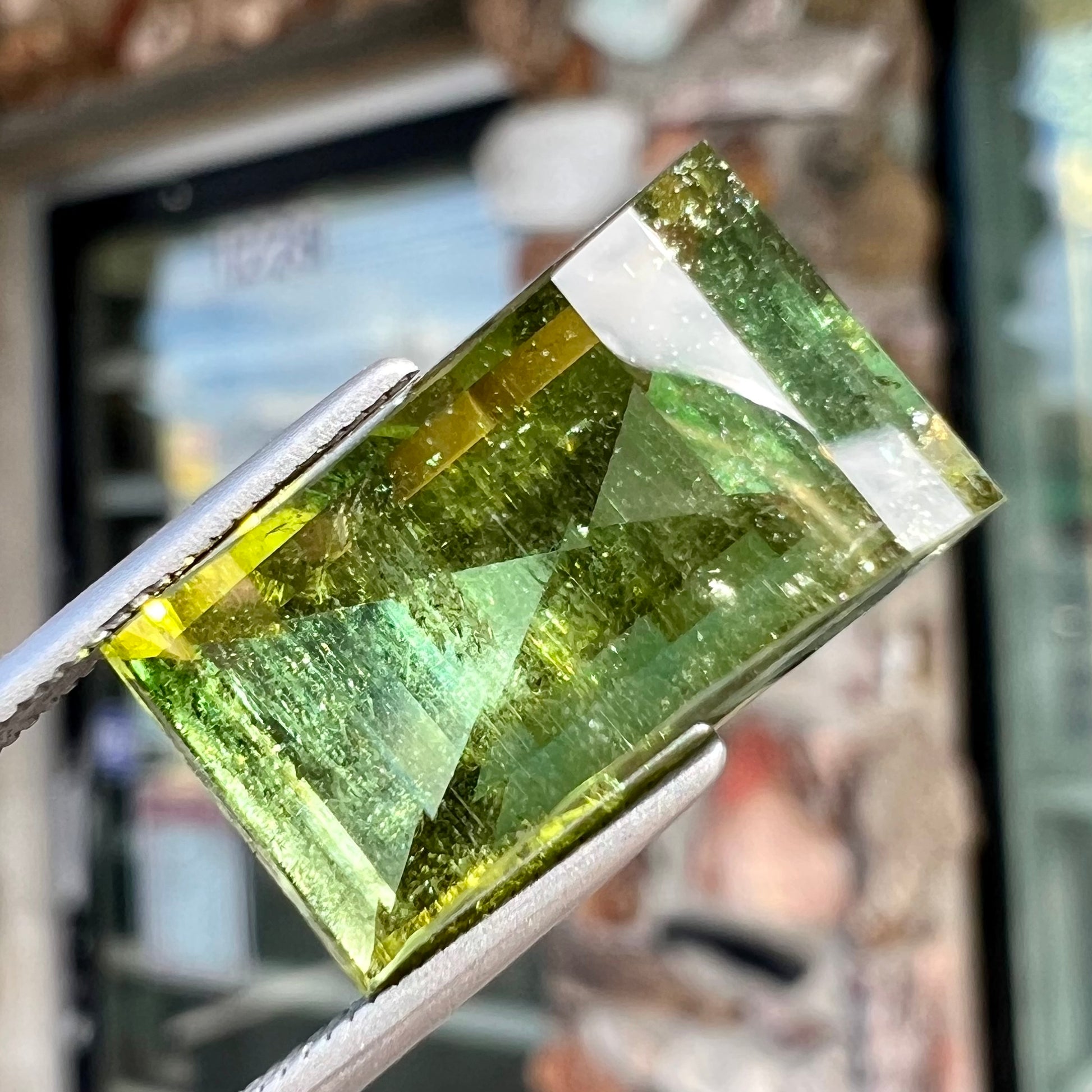 A rectangular step-cut yellowish green tourmaline gemstone.