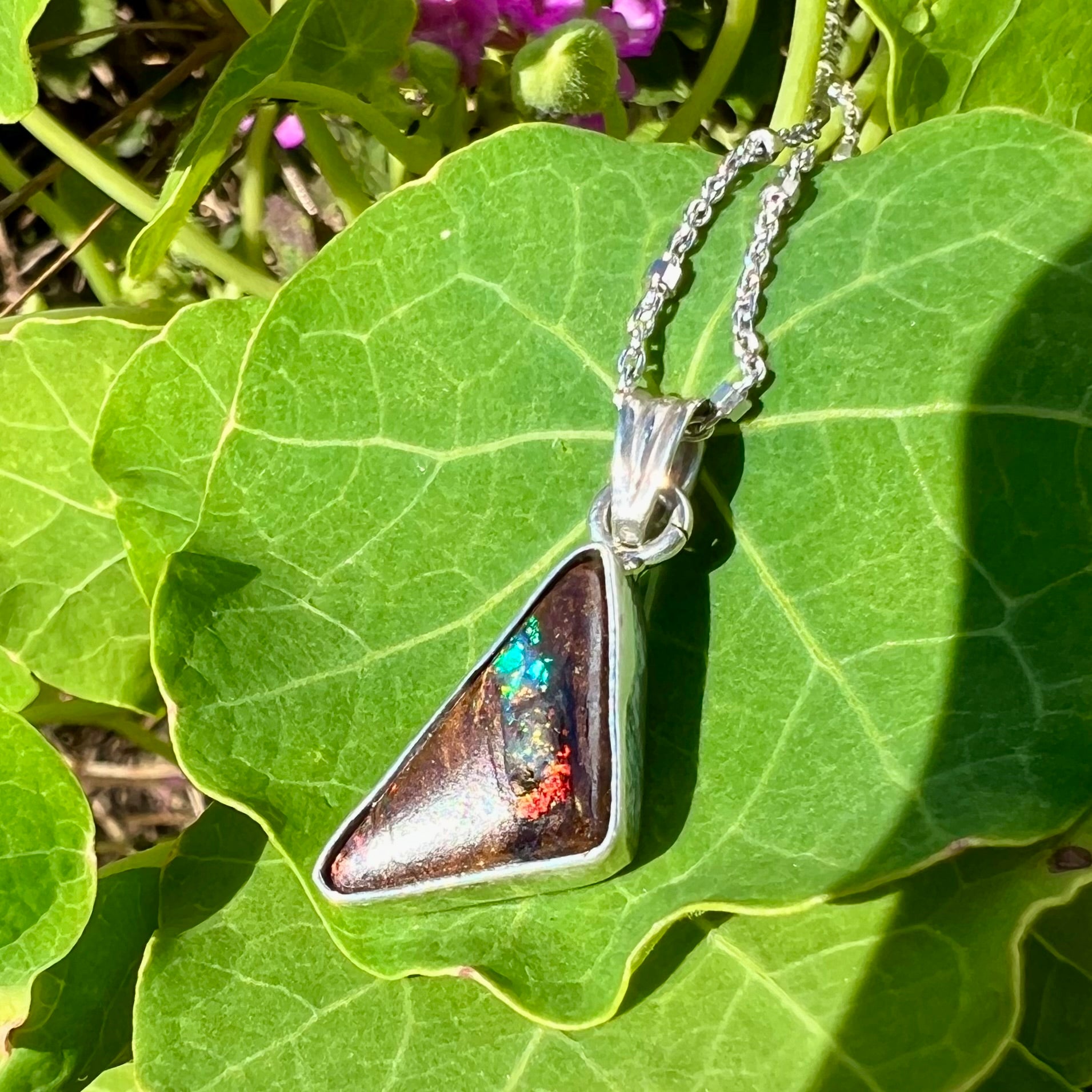 A sterling silver necklace bezel set with a triangle shaped boulder opal.  The opal has red and blue flashes.