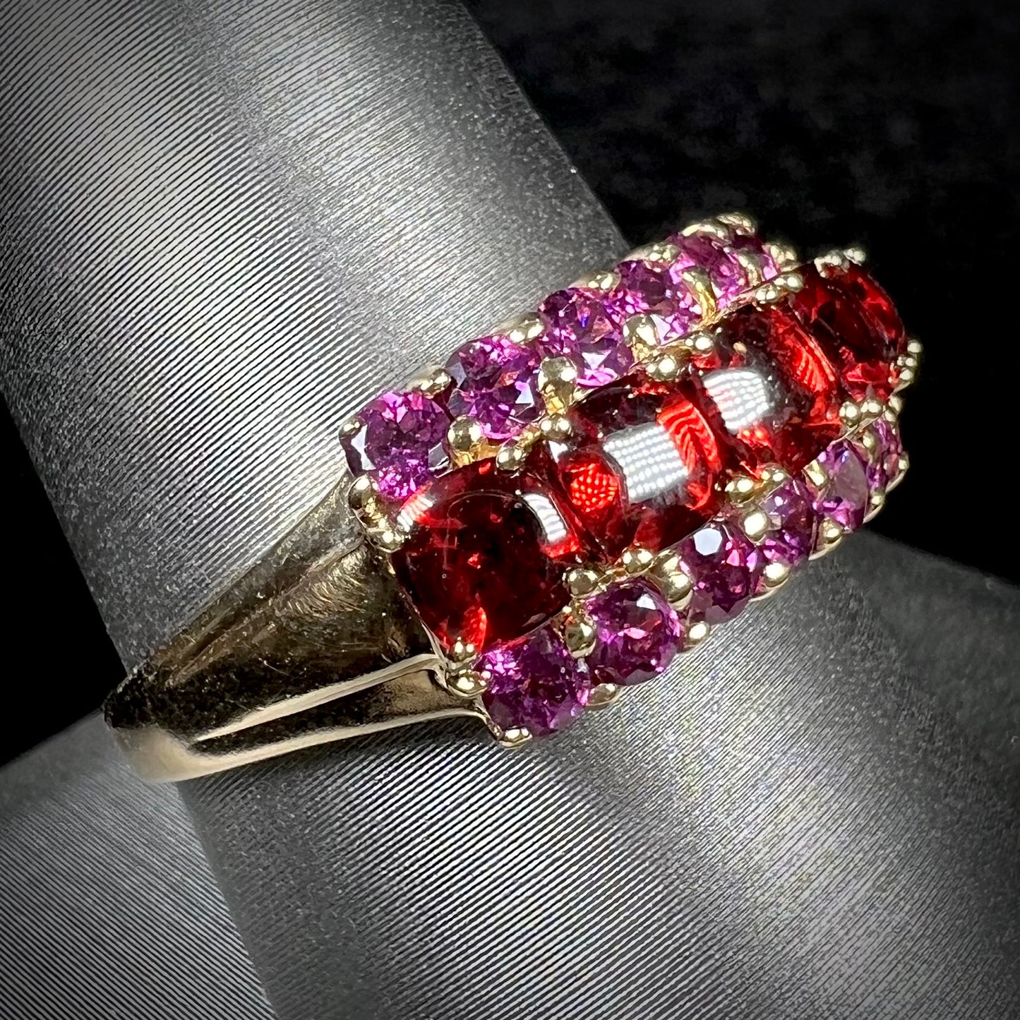 A gold ring set with buff cut cushion shaped almandine garnets with round cut purple rhodolite garnet accents.