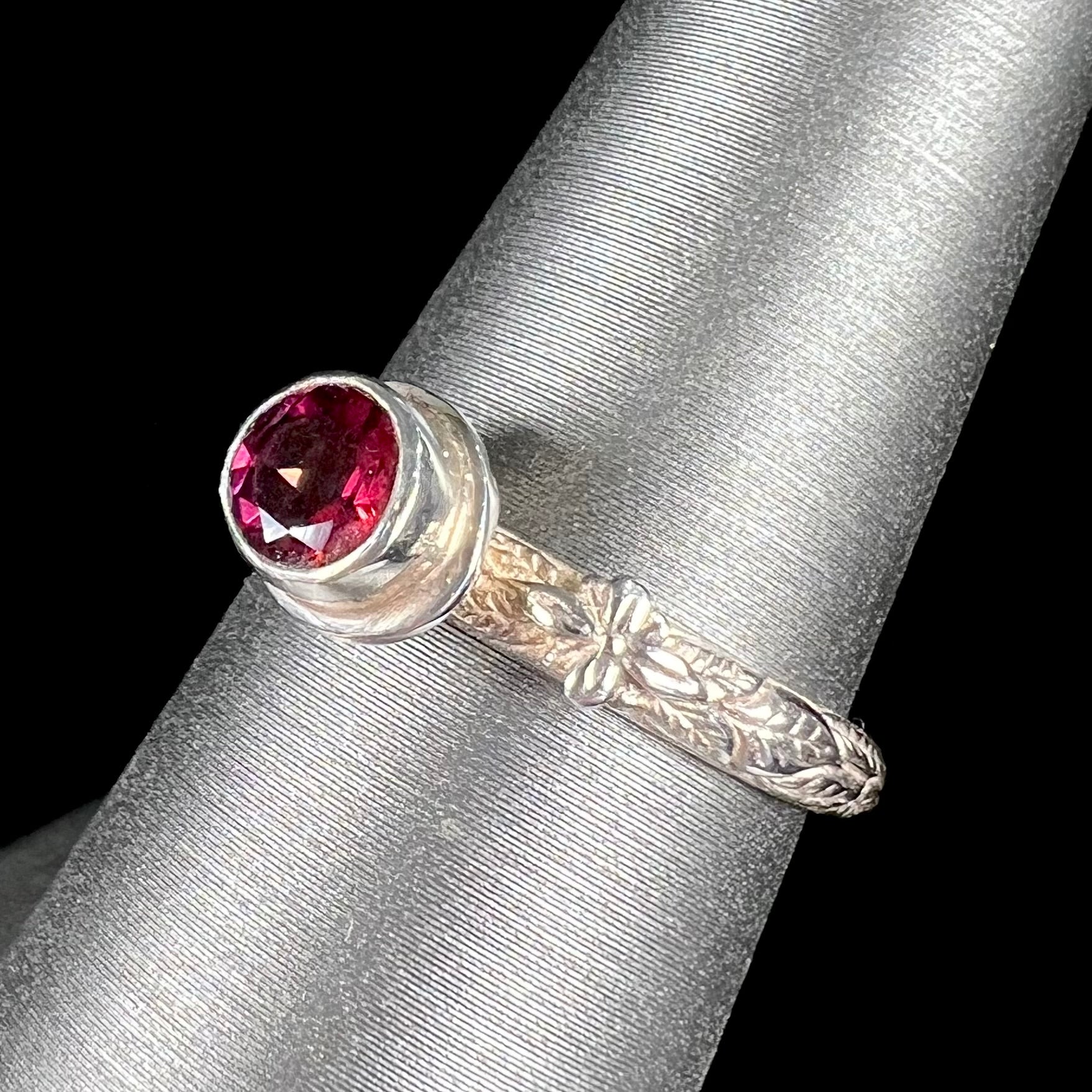 A ladies' sterling silver purple rhodonite garnet solitaire ring.  The shank has an etched floral leaf design.