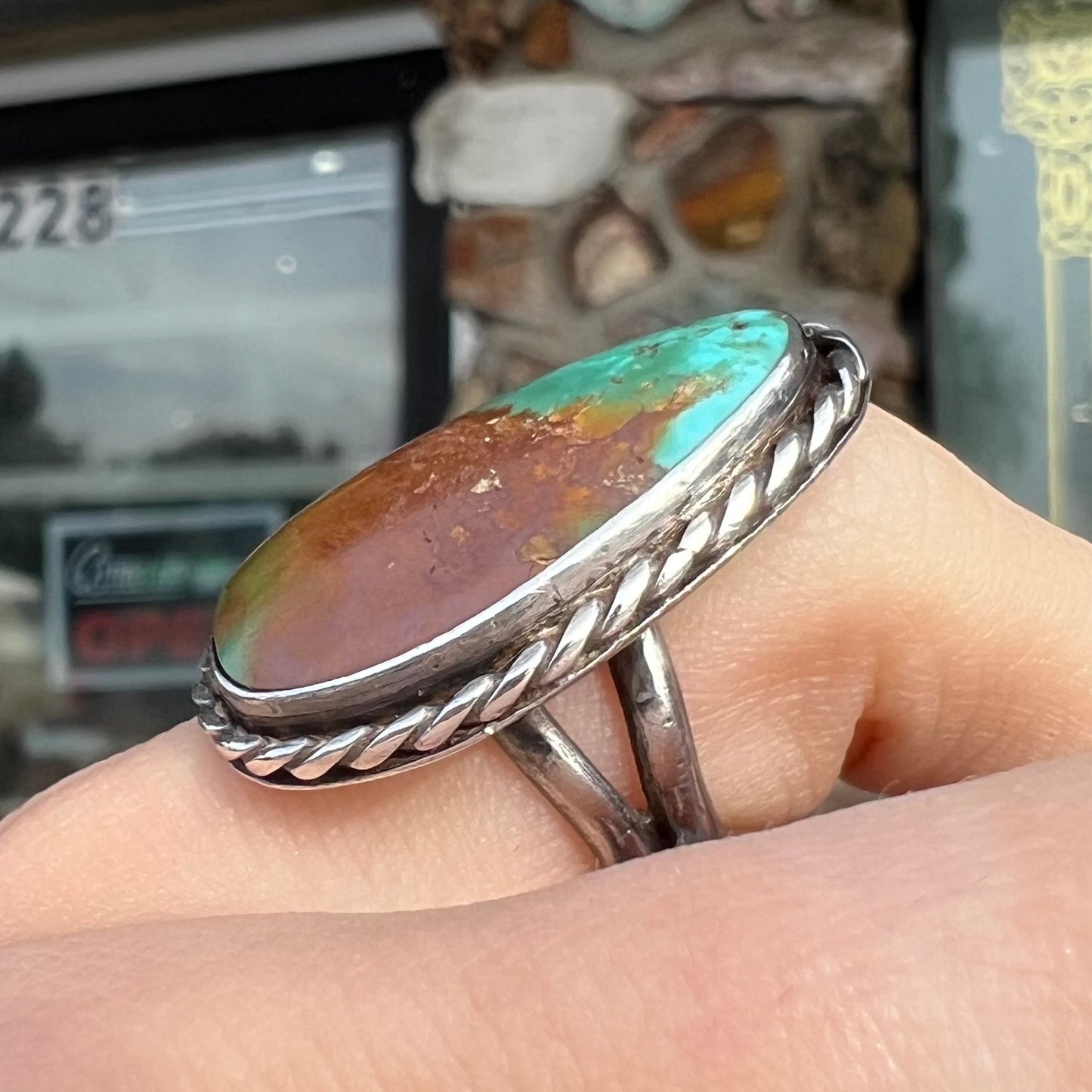 A sterling silver ring made with a rope bezel design and set with a green and brown Royston turquoise stone.