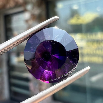 A modified round cut amethyst gemstone.  The stone is a dark bluish purple color.