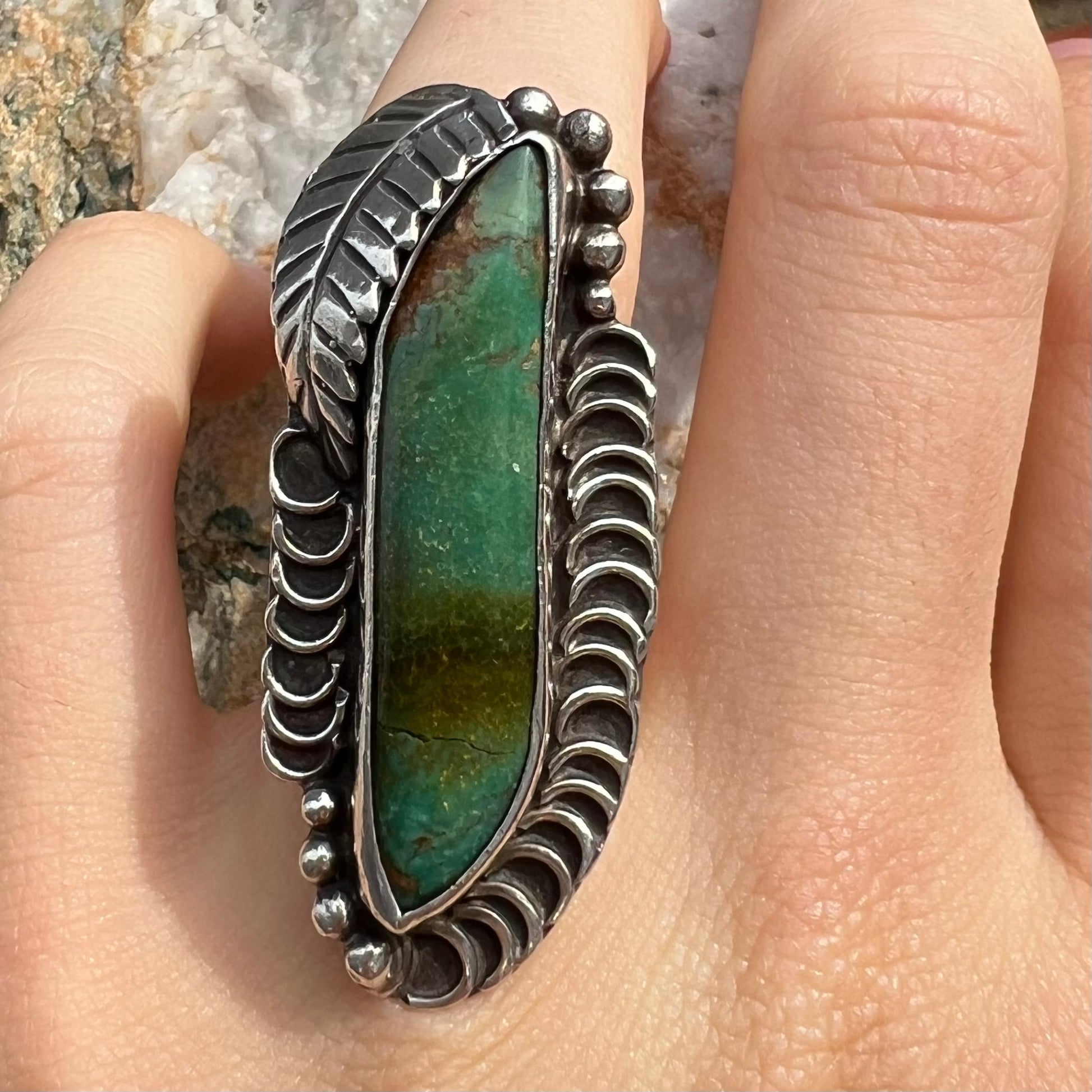 A sterling silver Navajo style ring set with a turquoise stone that shows colors of green, yellow, and reddish brown.