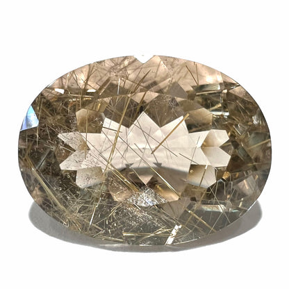 A faceted oval cut rutilated quartz gemstone.  The stone is smoky color with golden rutile needle inclusions.