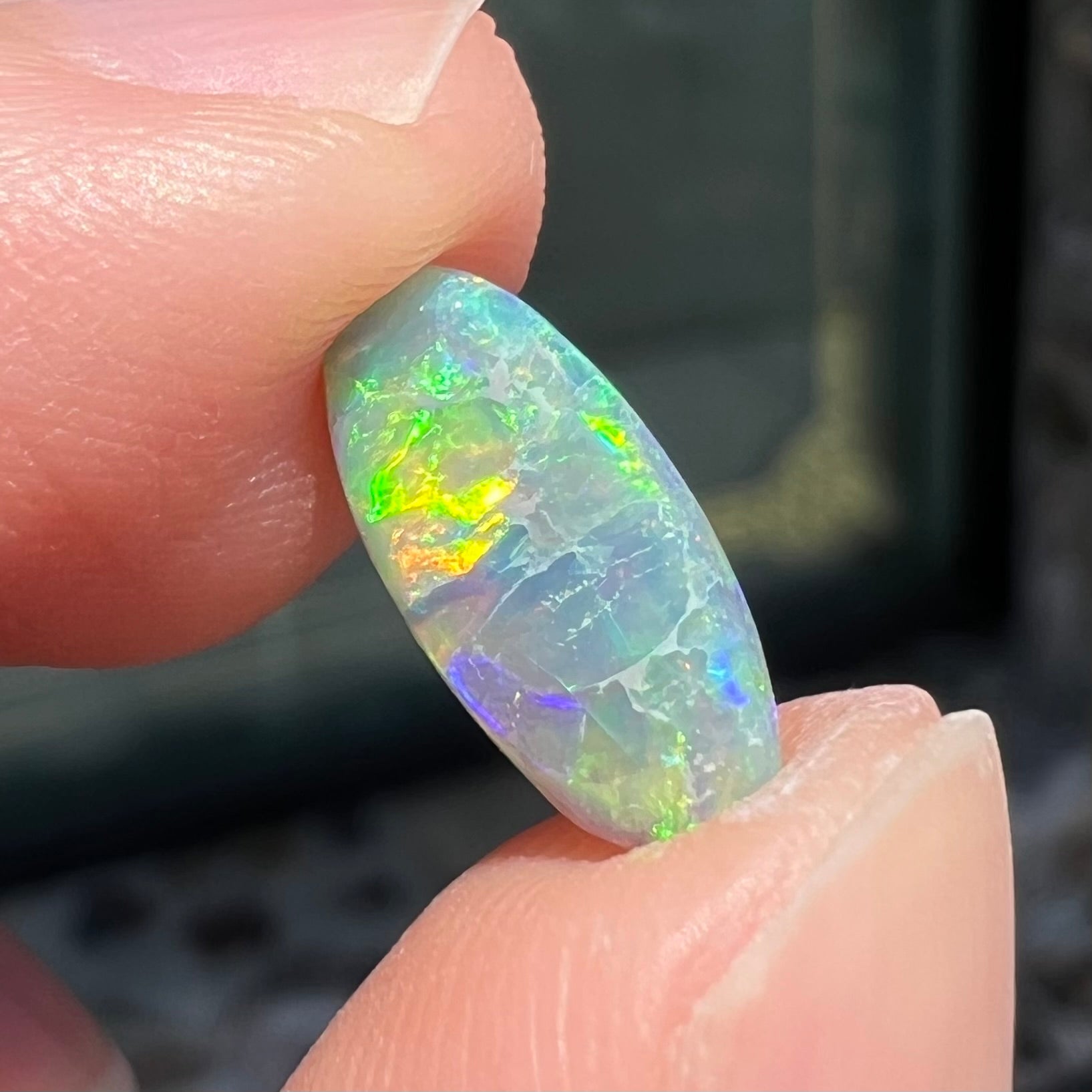 A loose, oval cabochon cut semi-black opal from Lightning Ridge, Australia.  The opal plays green and orange colors.