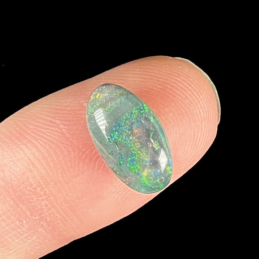 An oval cabochon cut semi-black opal stone from Lightning Ridge, Australia.