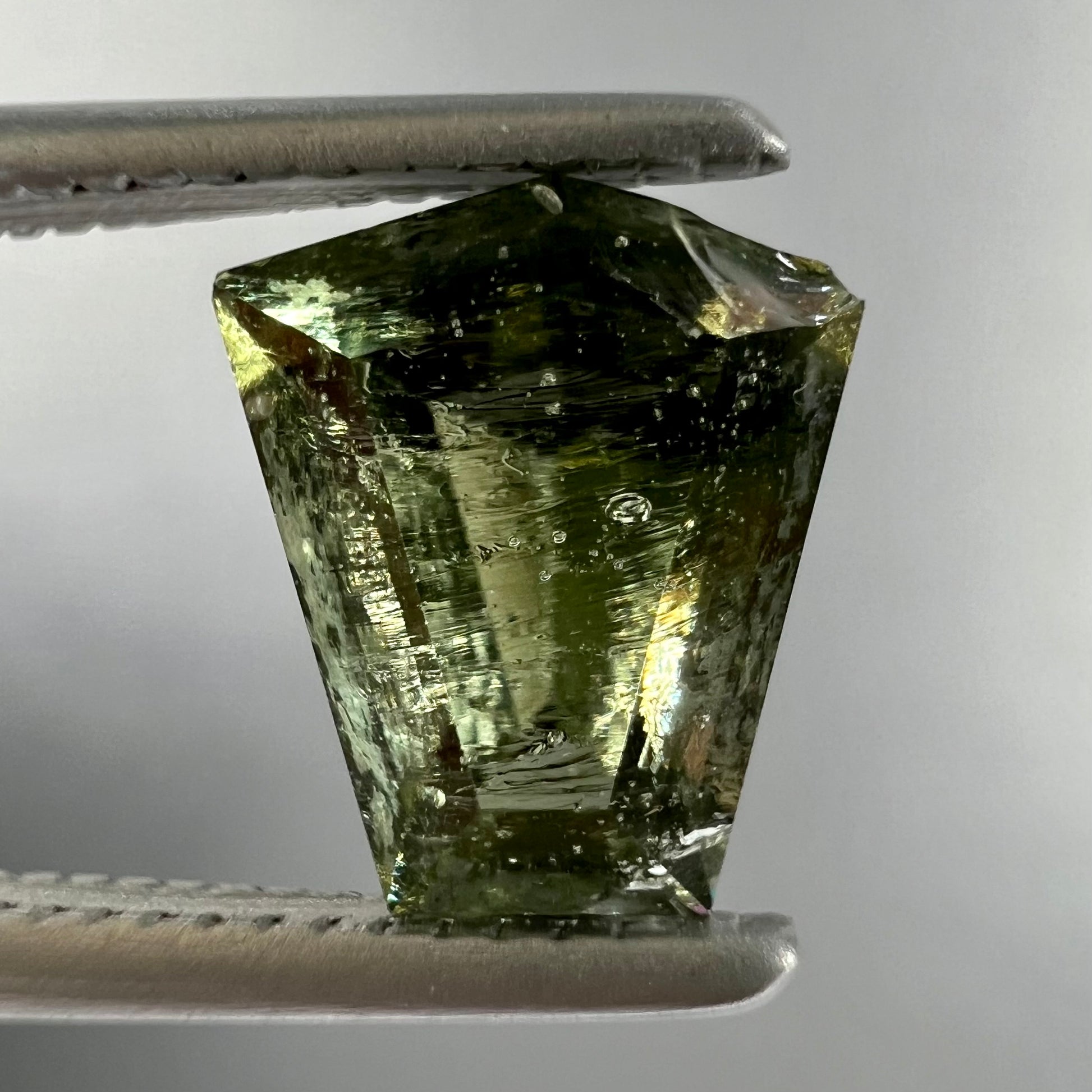 A loose, shield cut, natural moldavite gemstone.  The stone has a small chip in the top corner facet.