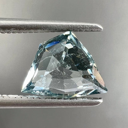 A loose, freeform shield cut tourmaline gemstone.  The stone is a steel blue color.