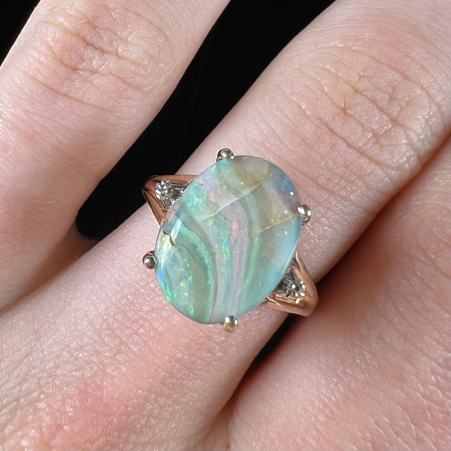 A ladies' Australian boulder opal ring set in yellow gold with diamond accents.  The opal shimmers green and pink and has fissure inclusions.