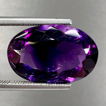 A loose, faceted oval cut Siberian amethyst gemstone.  The stone is purple color with blue and red flashes.