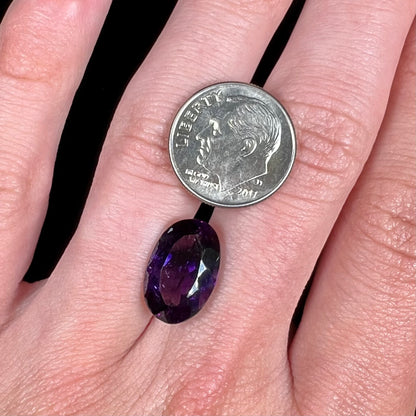 A loose, faceted oval cut Siberian amethyst gemstone.  The stone is purple color with blue and red flashes.