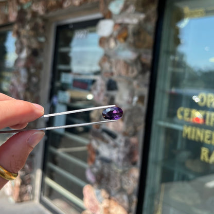 A loose, faceted oval cut Siberian amethyst gemstone.  The stone is purple color with blue and red flashes.