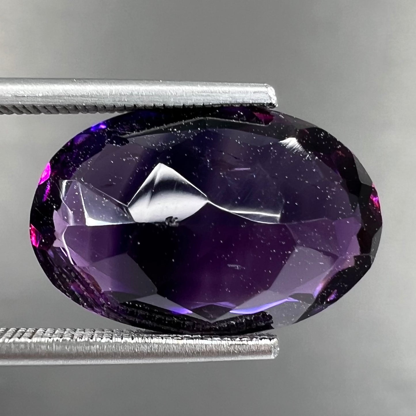 A loose, faceted oval cut Siberian amethyst gemstone.  The stone is purple color with blue and red flashes.