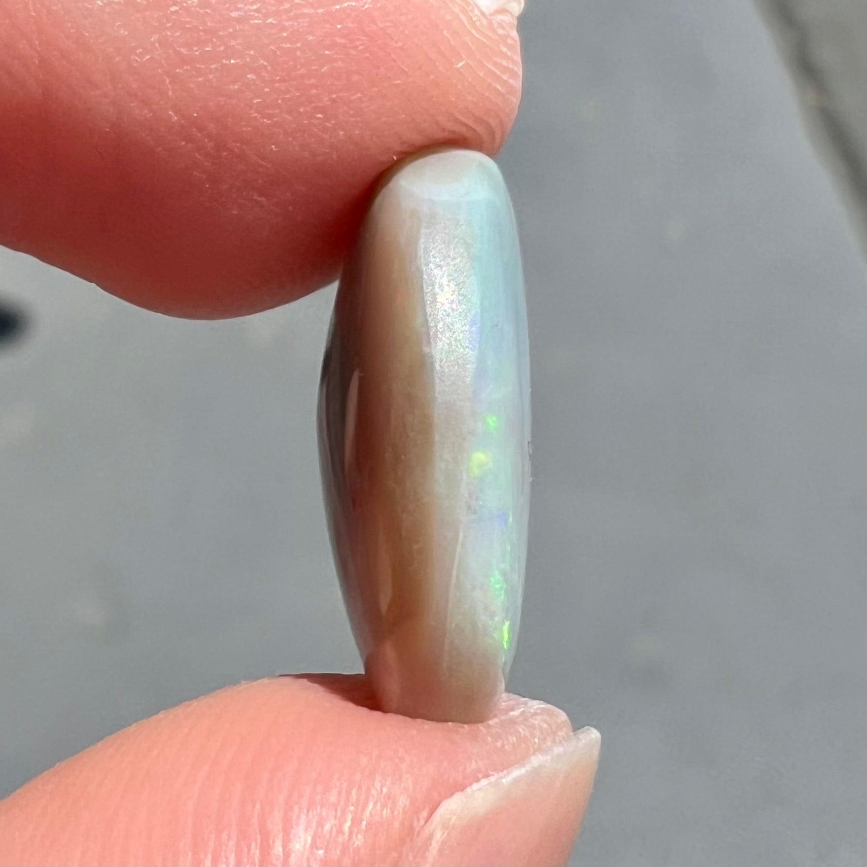 A loose, oval cut light opal stone from Mintabie, Australia.  The stone shows dull orange and green colors.