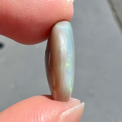A loose, oval cut light opal stone from Mintabie, Australia.  The stone shows dull orange and green colors.