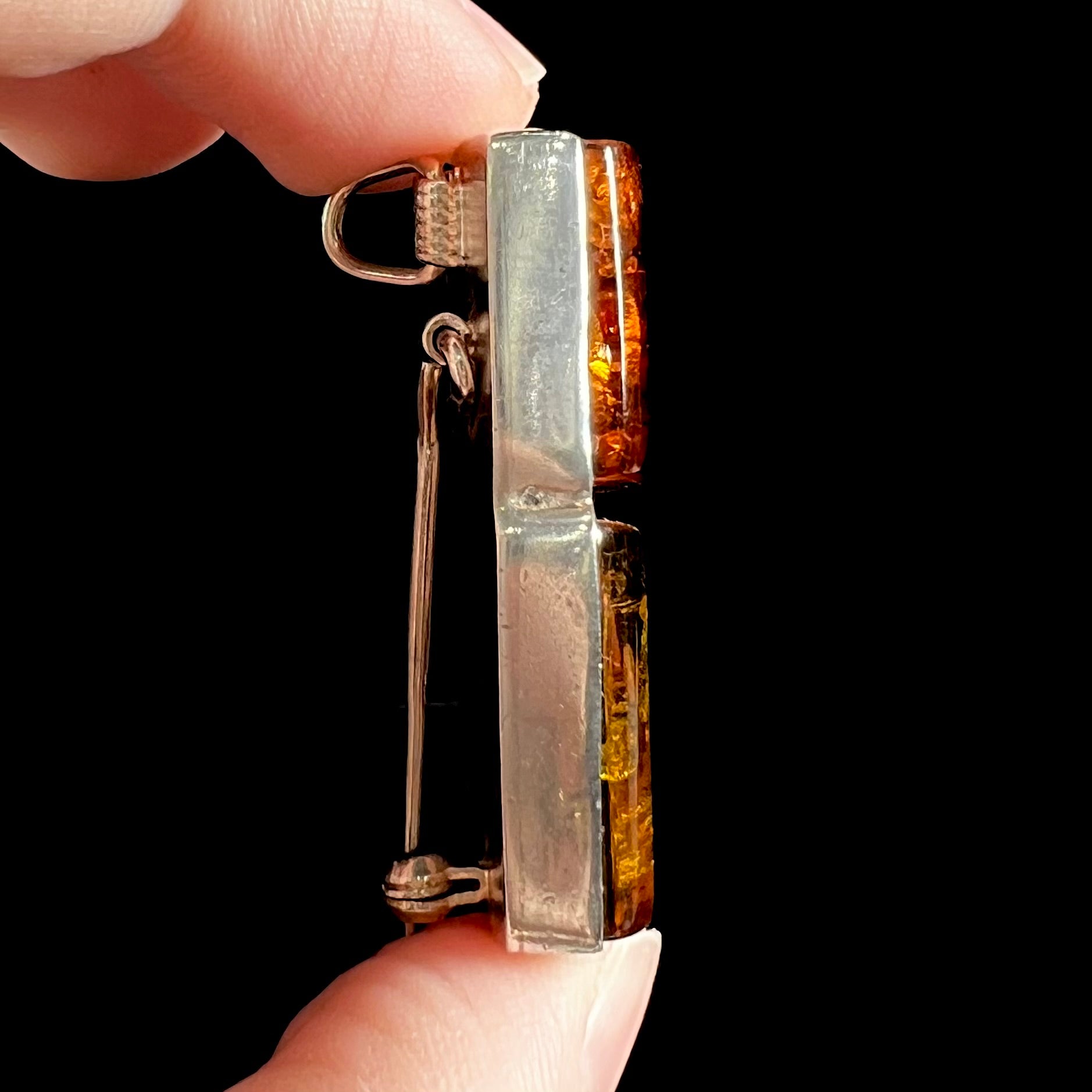 A sterling silver pendant brooch set with a red orange amber and a yellow sun-spangled amber.