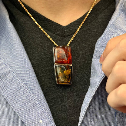 A sterling silver pendant brooch set with a red orange amber and a yellow sun-spangled amber.