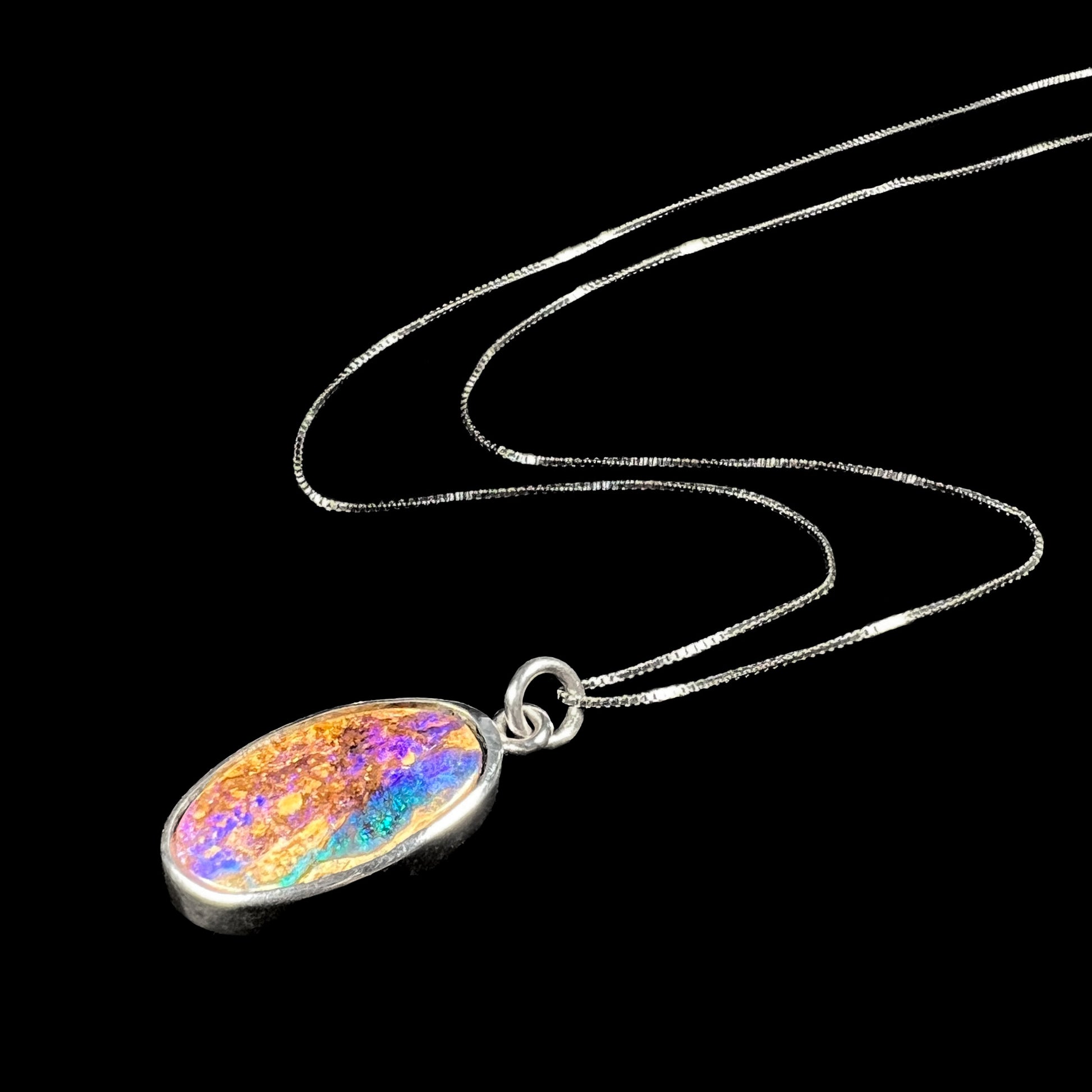 A handmade sterling silver pendant bezel set with an oval cut pipe boulder opal stone.