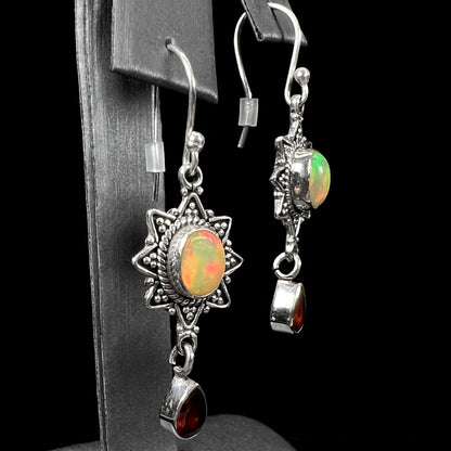 A pair of sterling silver star design dangle earrings set with Ethiopian fire opals and pear shaped red garnet accents.