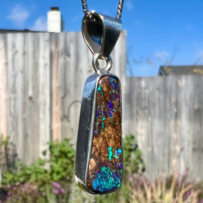 An elongated shaped natural boulder opal necklace in sterling silver.  The opal flashes bright blue and green colors.