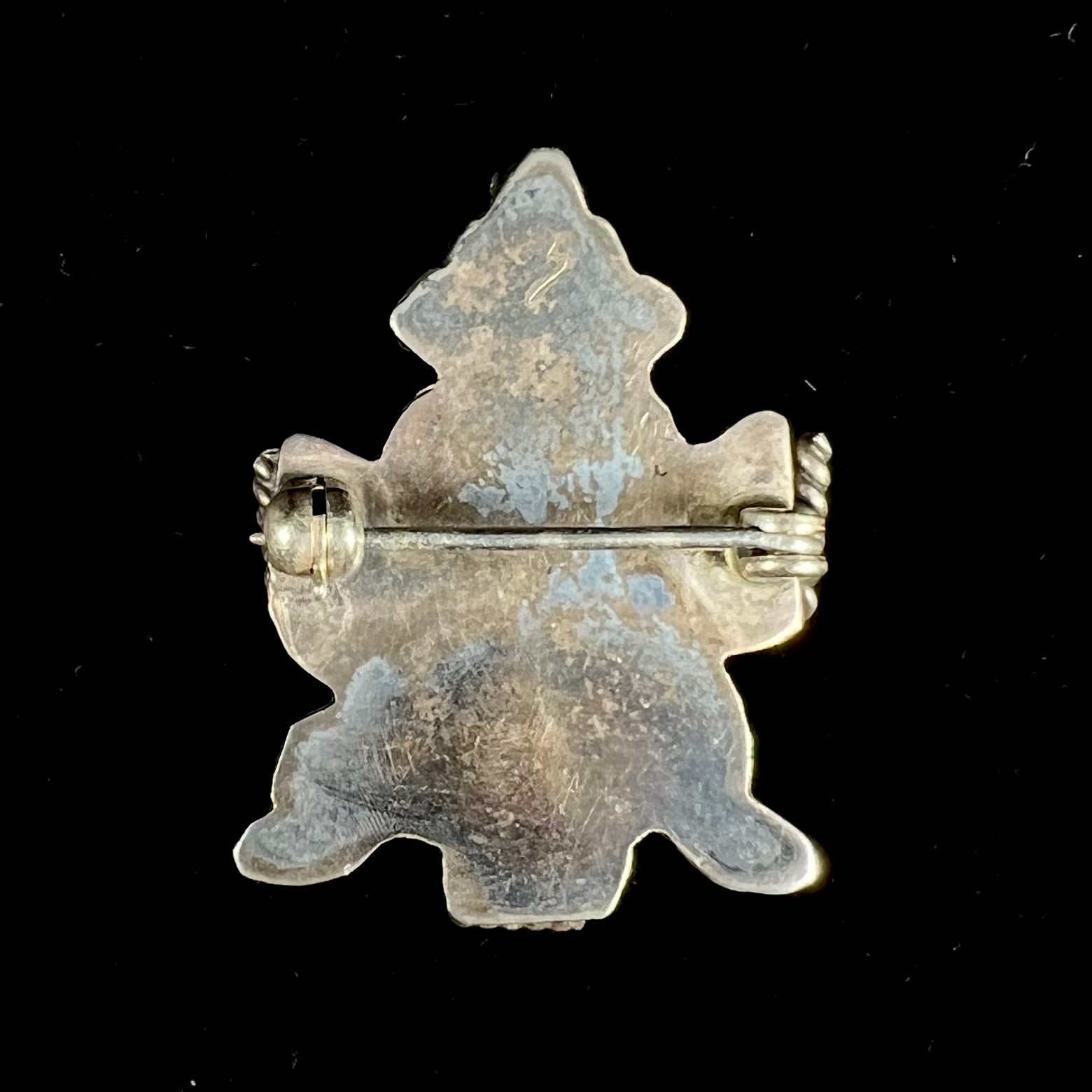 A sterling silver brooch depicting a Zuni Indian knifewing dancer, inlaid with jet, turquoise, coral, and mother of pearl.