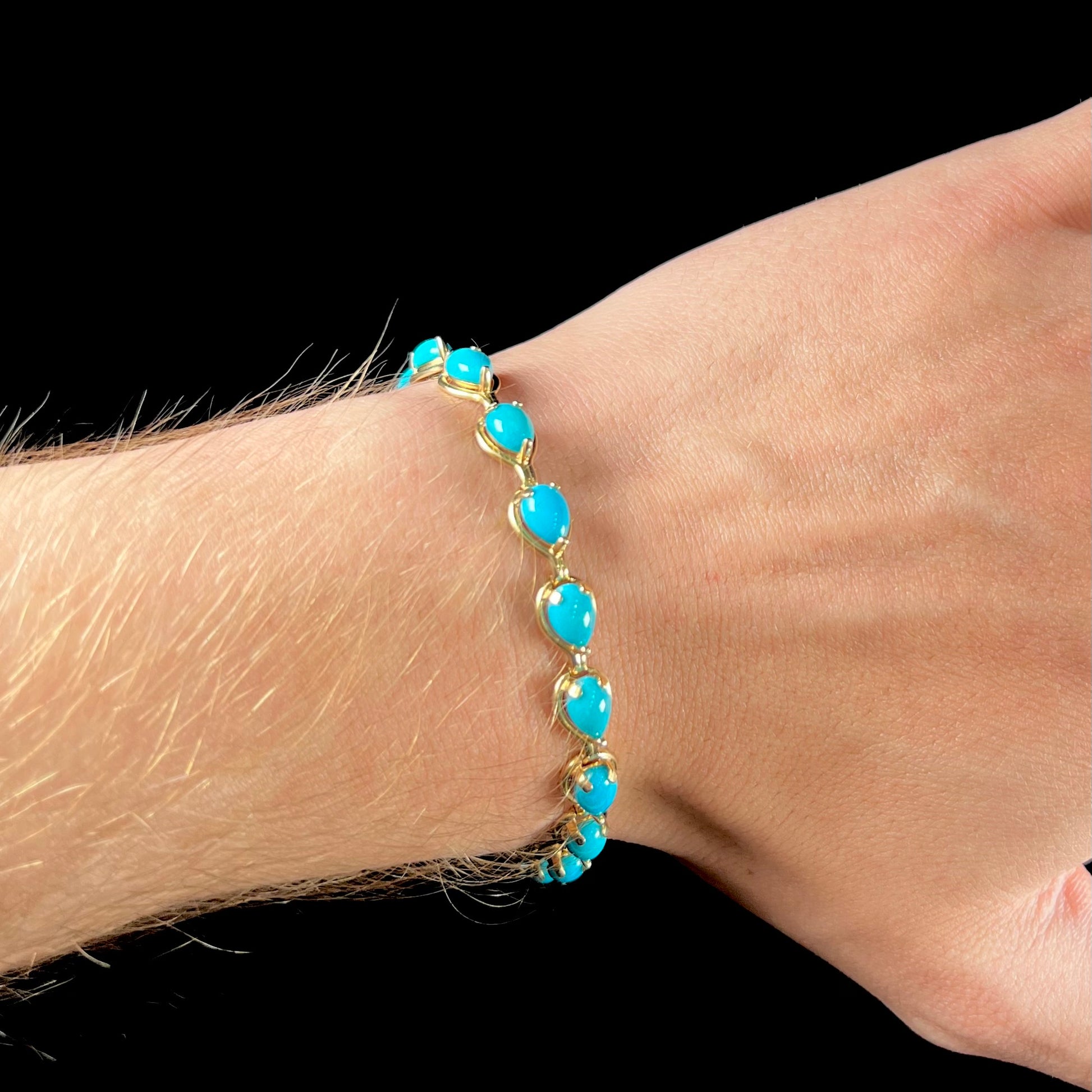A ladies' yellow gold tennis style bracelet set with pear cabochon shaped natural Sleeping Beauty turquoise stones.