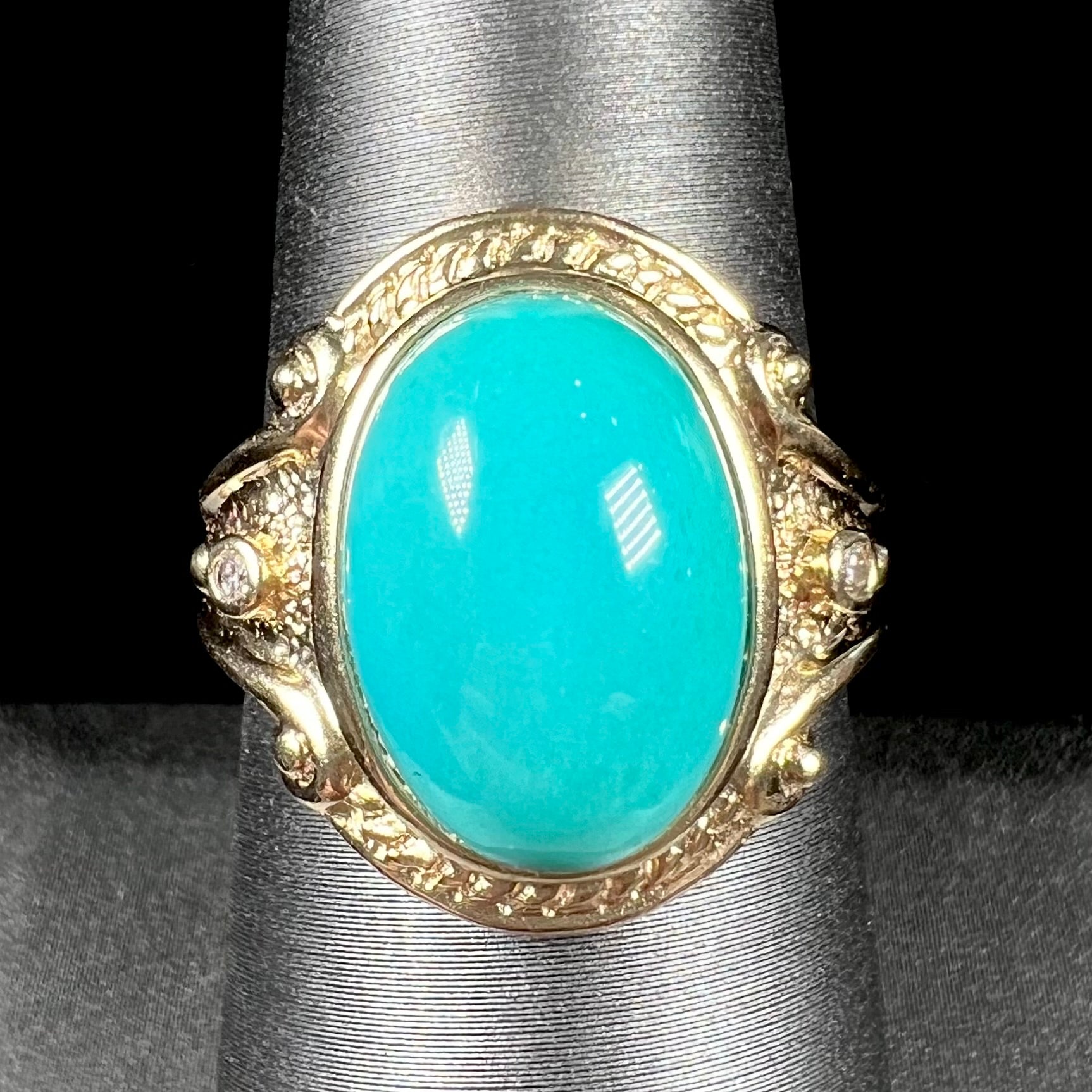 A yellow gold ring set with a greenish blue Sleeping Beauty turquoise cabochon with two diamond accents.