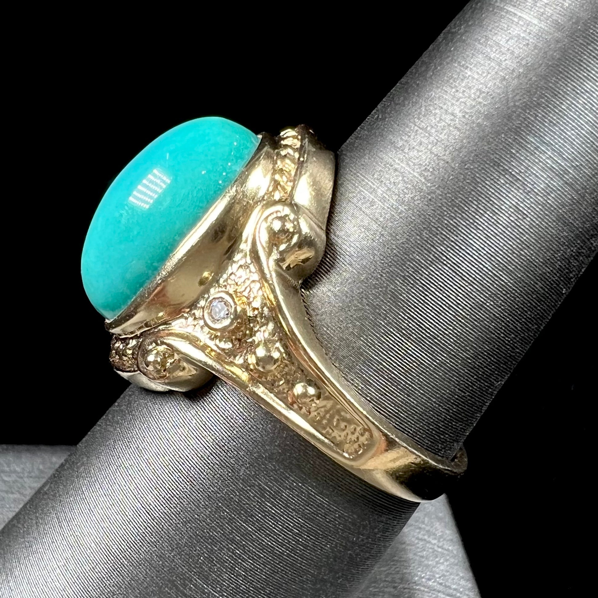 A yellow gold ring set with a greenish blue Sleeping Beauty turquoise cabochon with two diamond accents.
