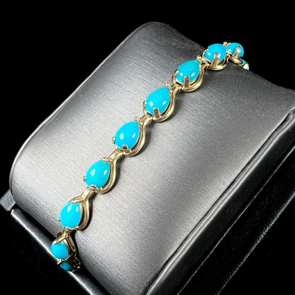 A ladies' yellow gold tennis style bracelet set with pear cabochon shaped natural Sleeping Beauty turquoise stones.