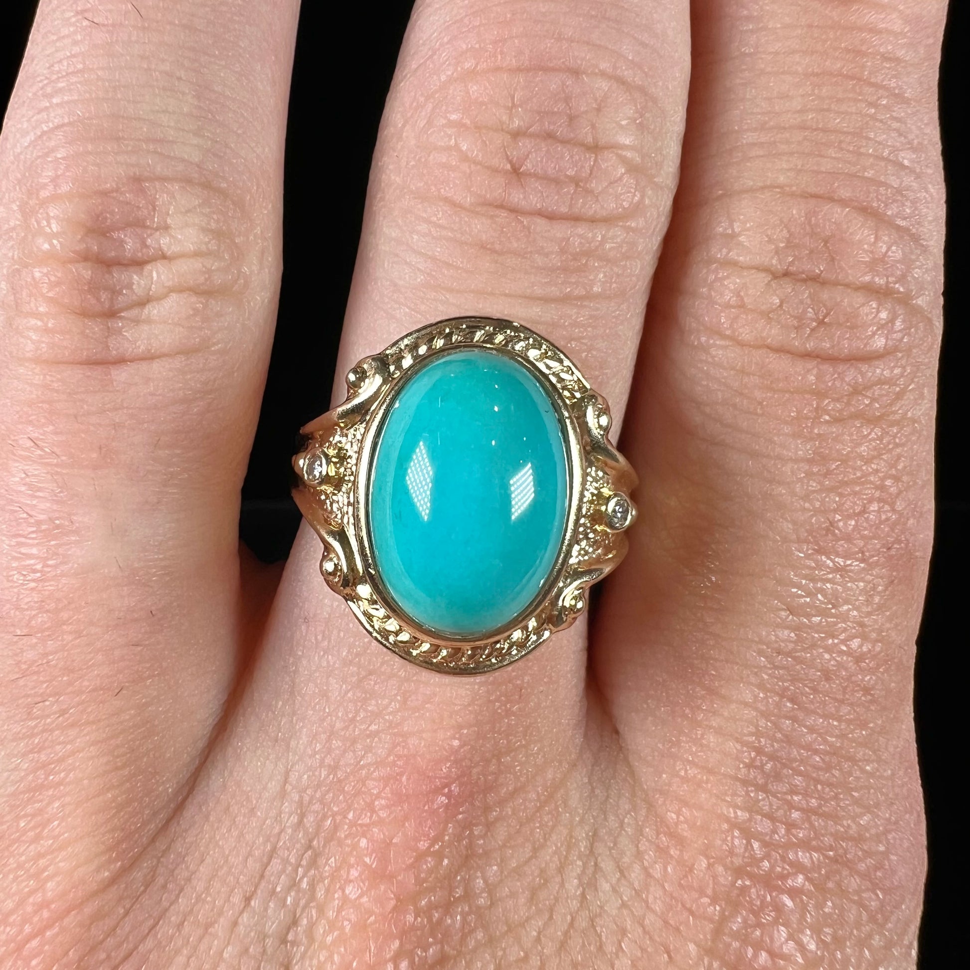 A yellow gold ring set with a greenish blue Sleeping Beauty turquoise cabochon with two diamond accents.