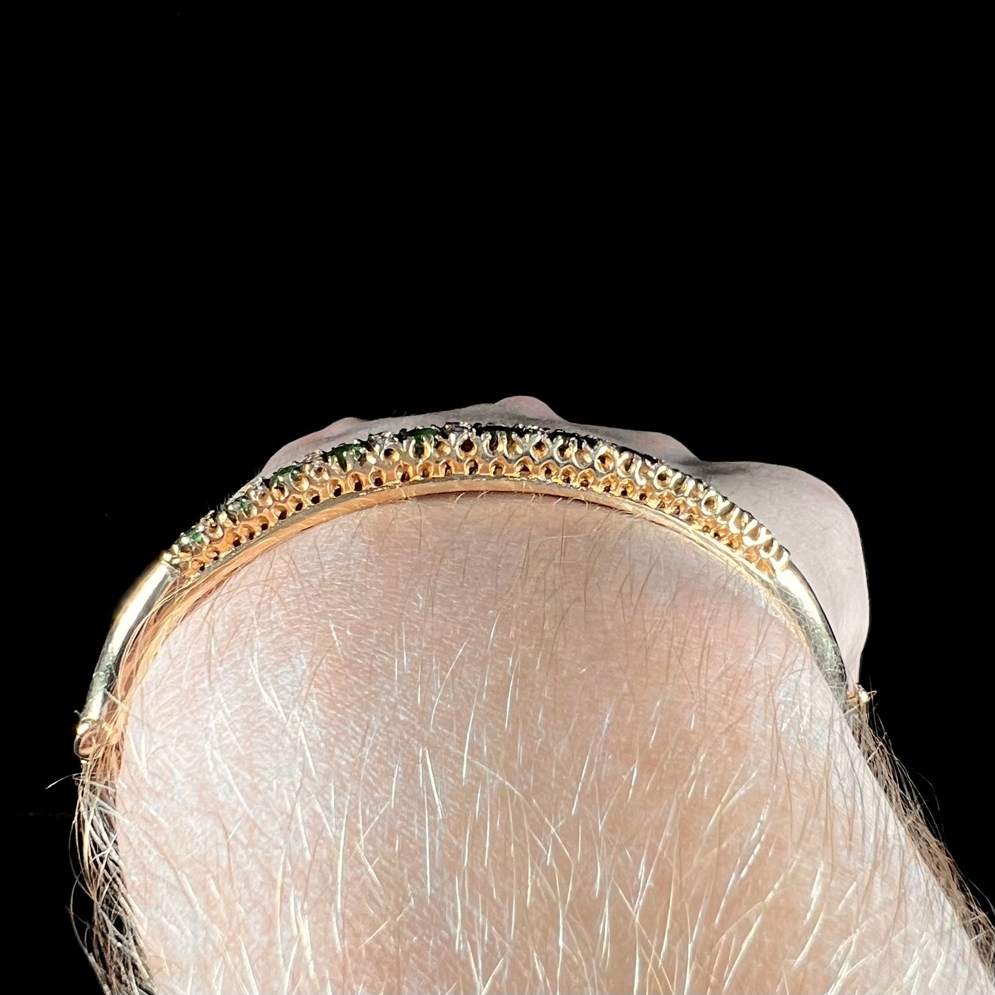 A ladies' yellow gold bangle bracelet set with round cut emeralds and diamonds.