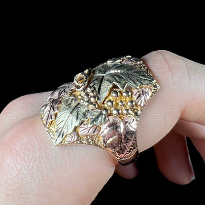 A men's solid gold ring.  The ring is Black Hills gold featuring a grapevine and leaf motif with rose and green gold designs.